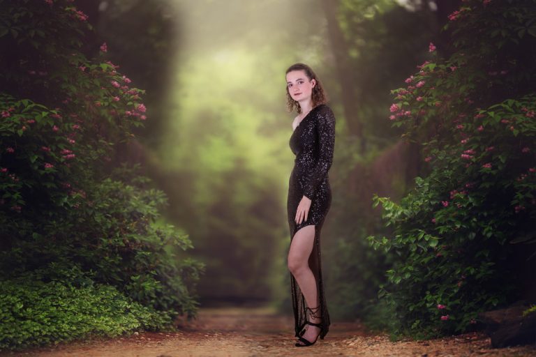 fine art portrait of a teen girl dressed in black formal dress standing in green forest by katja photography