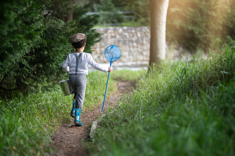 Portrait of a young boy running away holding a fishing net and bucket by Katja Photography