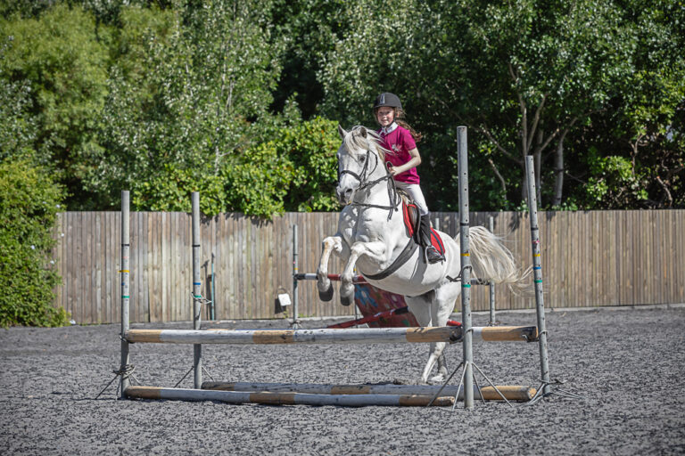 Outdoor portrait of a young girl riding her pony over a jump by Katja Photography