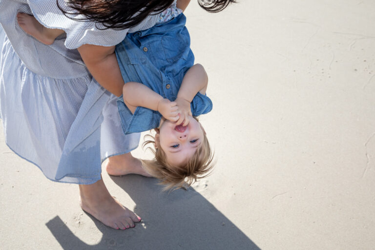 Mother playfully holding young daughter upside down by Katja Photography