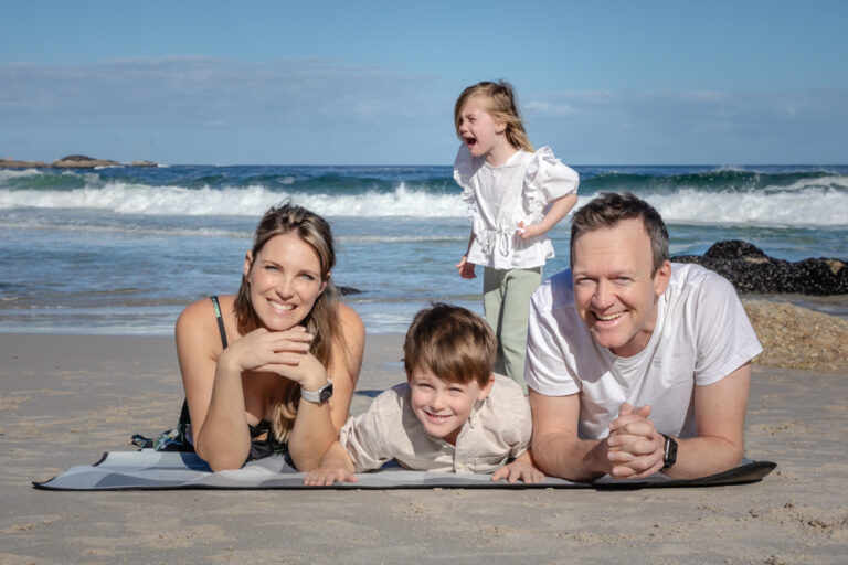 Family posing on the beach while daughter cries in the background by Katja Photography