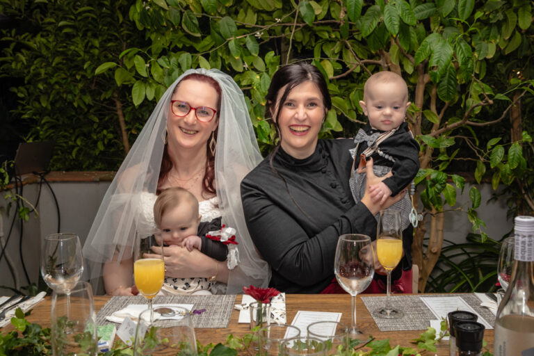 Trans couple at wedding holding babies by Katja Photography